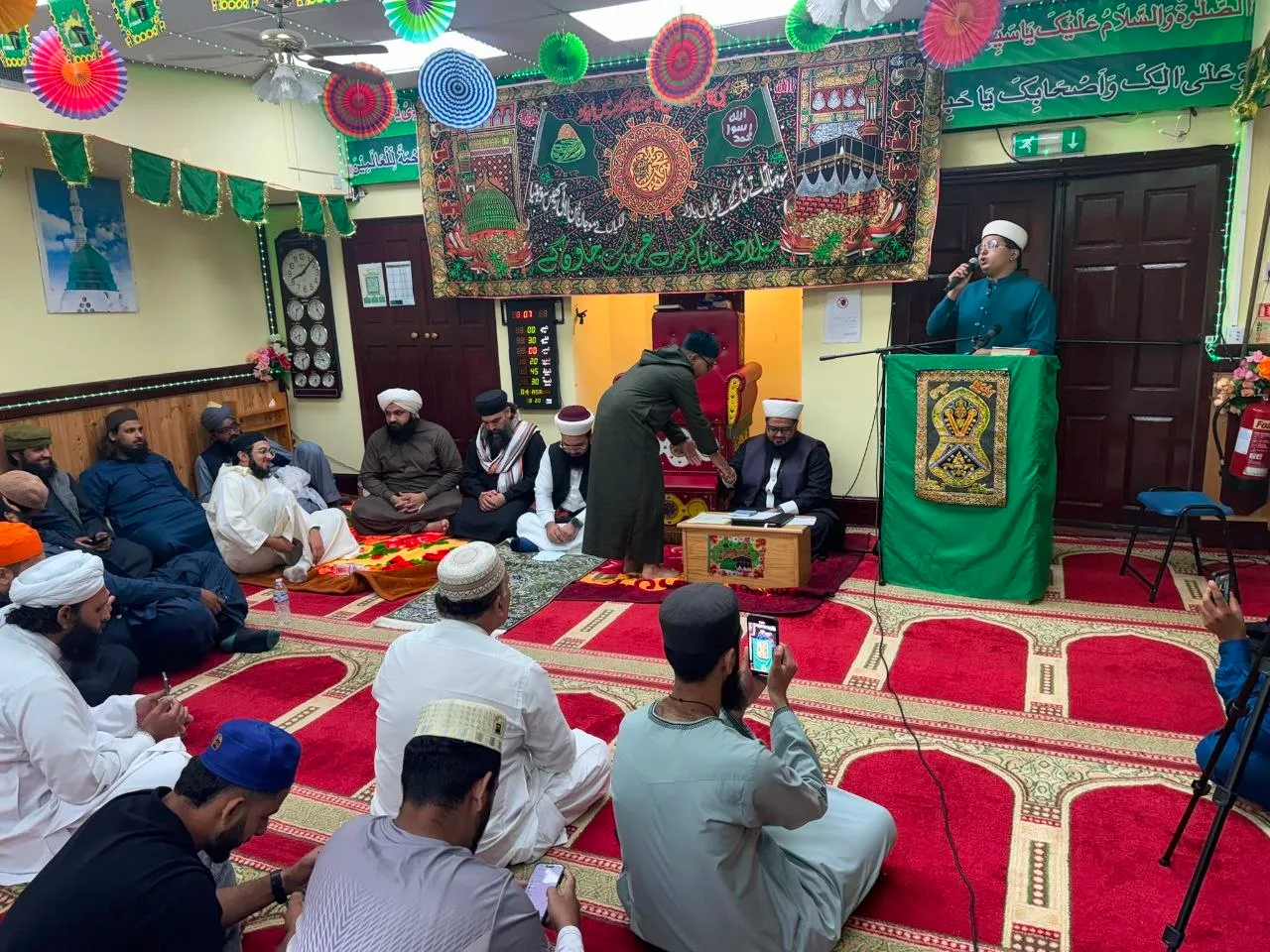 Na’at recited at the lectern during the Annual Mawlid-un-Nabi at Ghousia Masjid, with scholars seated beneath a banner of the Green Dome and the Ka’bah